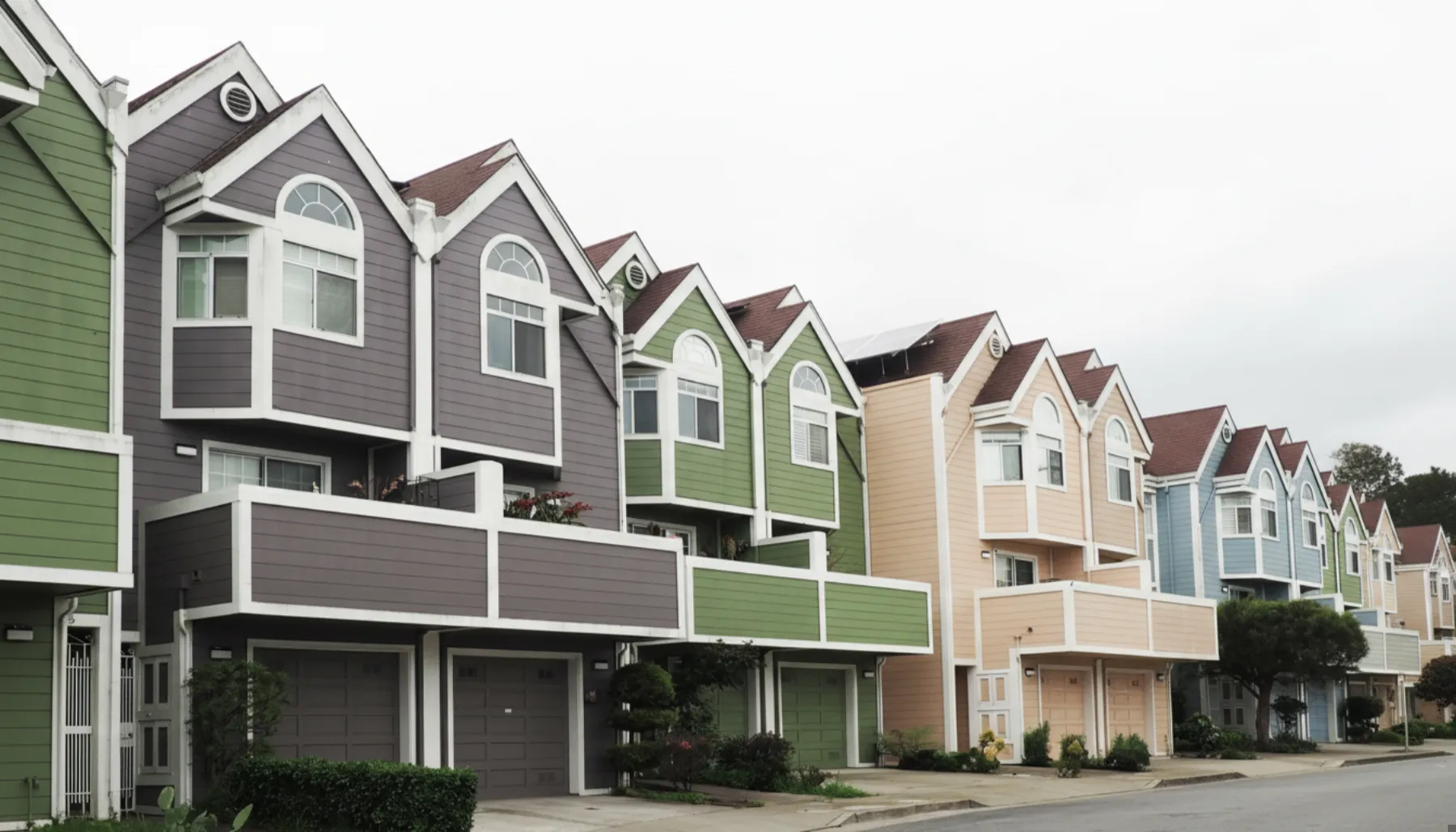 A row of modern, multi-story townhouses with different colored exteriors including purple, green, peach, and blue, under an overcast sky.