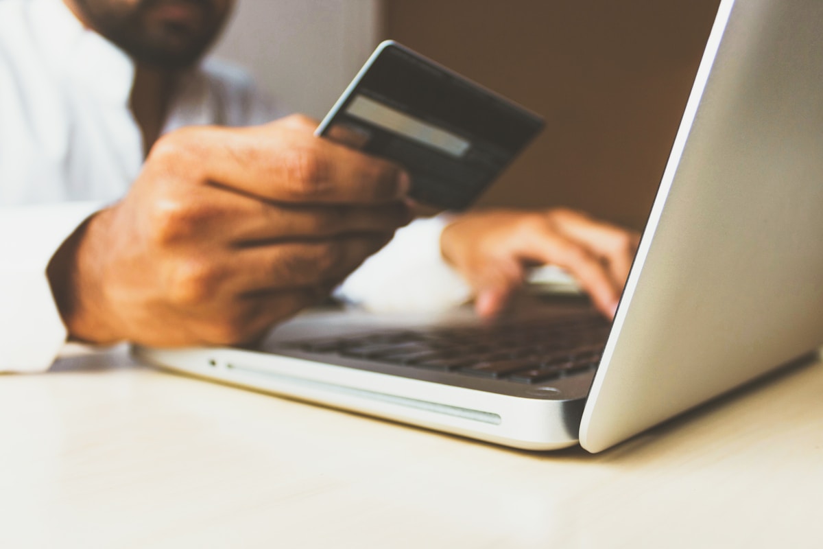 A person holds a credit card in one hand while typing on a laptop with the other, suggesting an online payment or shopping activity.