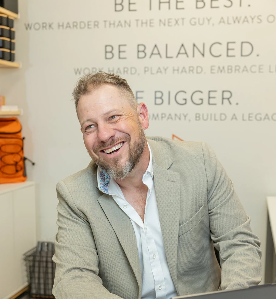 Jordi Browne laughing at his laptop in the Browne Mortgage office