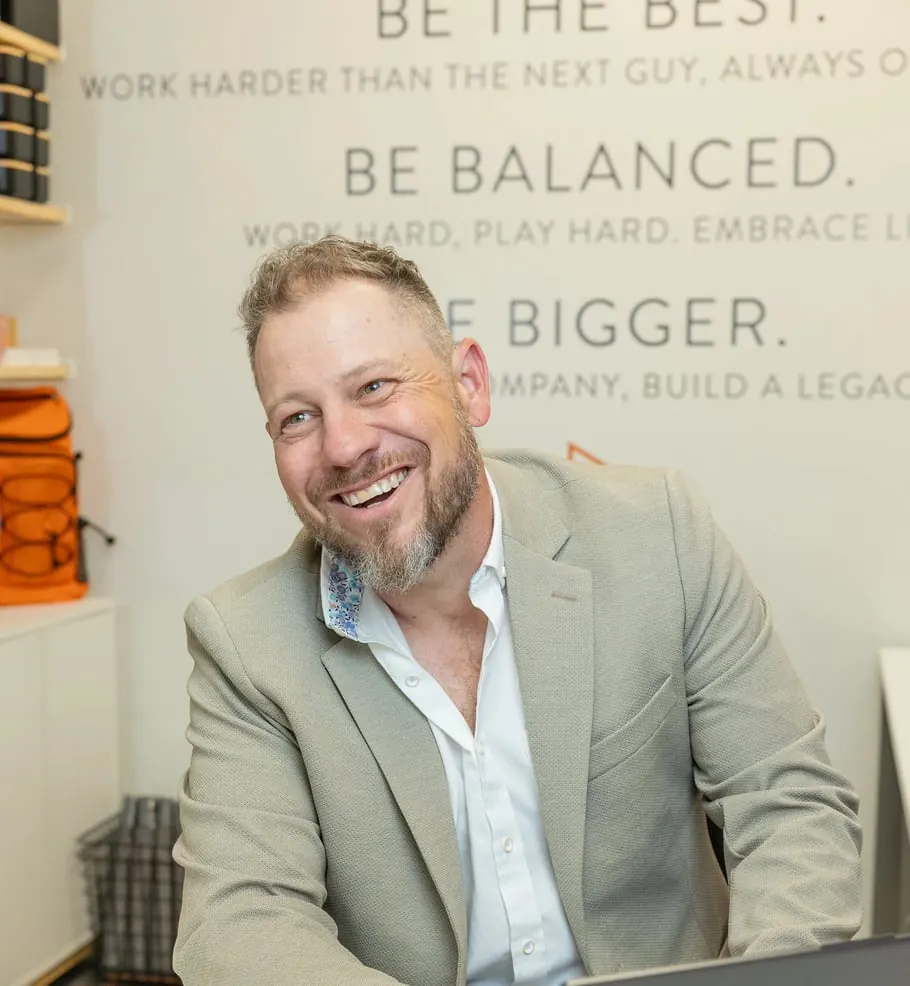 Jordi Browne laughing at his laptop in the Browne Mortgage office