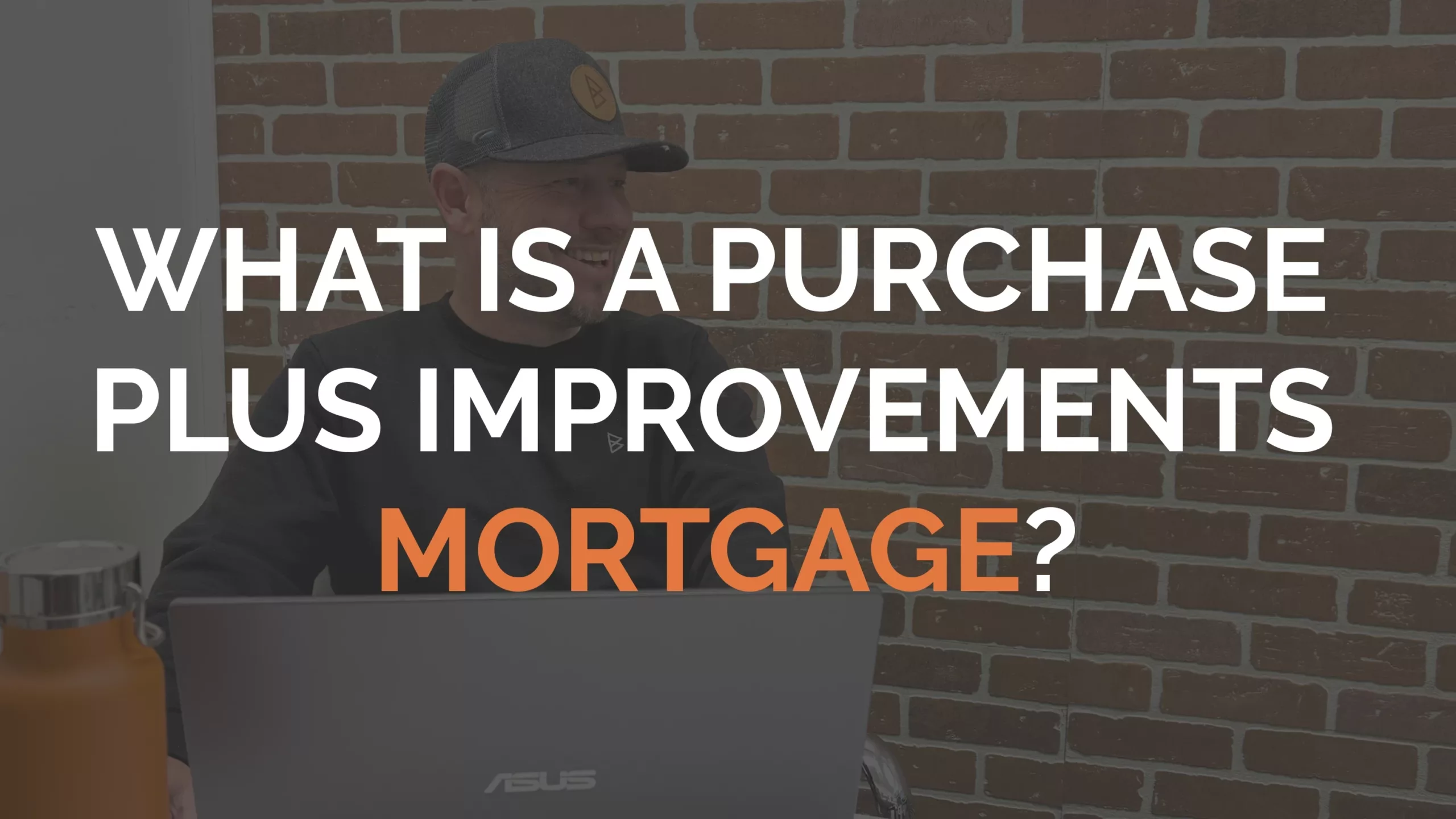 Man sitting at a desk with a laptop in front of a brick wall; text overlay reads "What is a purchase plus improvements mortgage?.