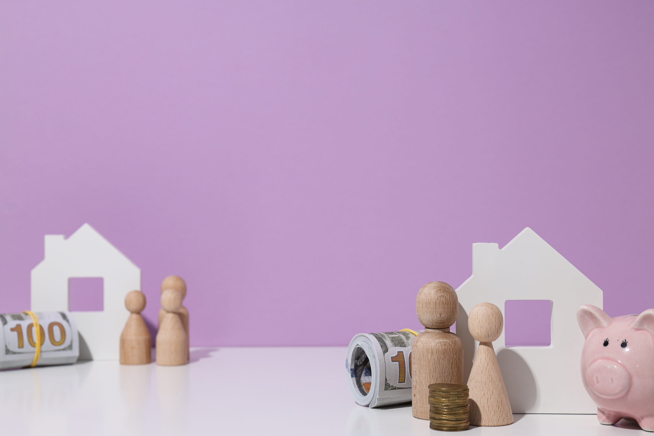 Wooden houses, money, piggy bank and wooden figures on purple ba