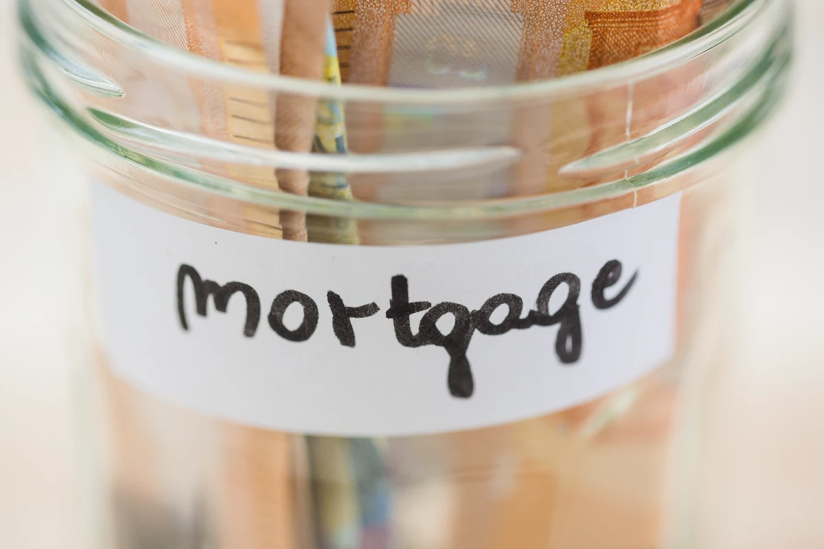 Glass jar labeled "mortgage" containing assorted paper currency.